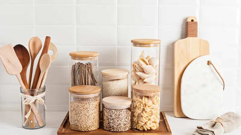 Glass storage jars of pasta and grains beside wooden kitchen utensils